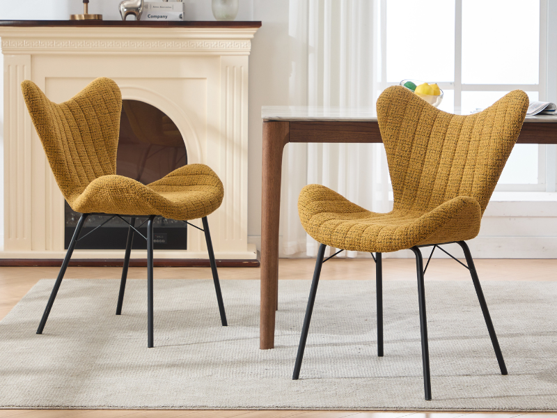 Silla decorativa moderna con respaldo lateral en tapicería de color amarillo mostaza con patas de metal oscuro, que se muestra desde varios ángulos en un ambiente interior luminoso.