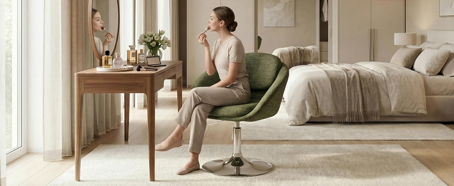 Woman sitting in green armchair in modern bedroom with beige bedding, wooden side table with flowers, and bright windows with neutral décor.