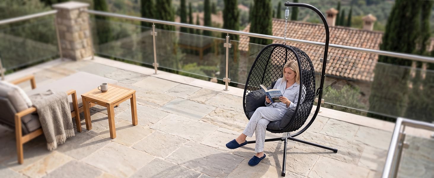 Sedia a uovo sospesa nera con imbottitura montata su supporto in patio esterno con tavolo in legno e ringhiera in metallo a vista.