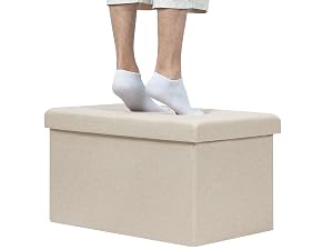 Pouf o scatola portaoggetti in tessuto beige con qualcuno che indossa calzini bianchi alla caviglia in piedi sopra, a dimostrazione della sua