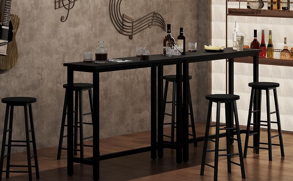 Industrial-style bar setup with high wooden table, black metal stools, and hanging light fixtures. Bottles and glassware visible on shelves in background.