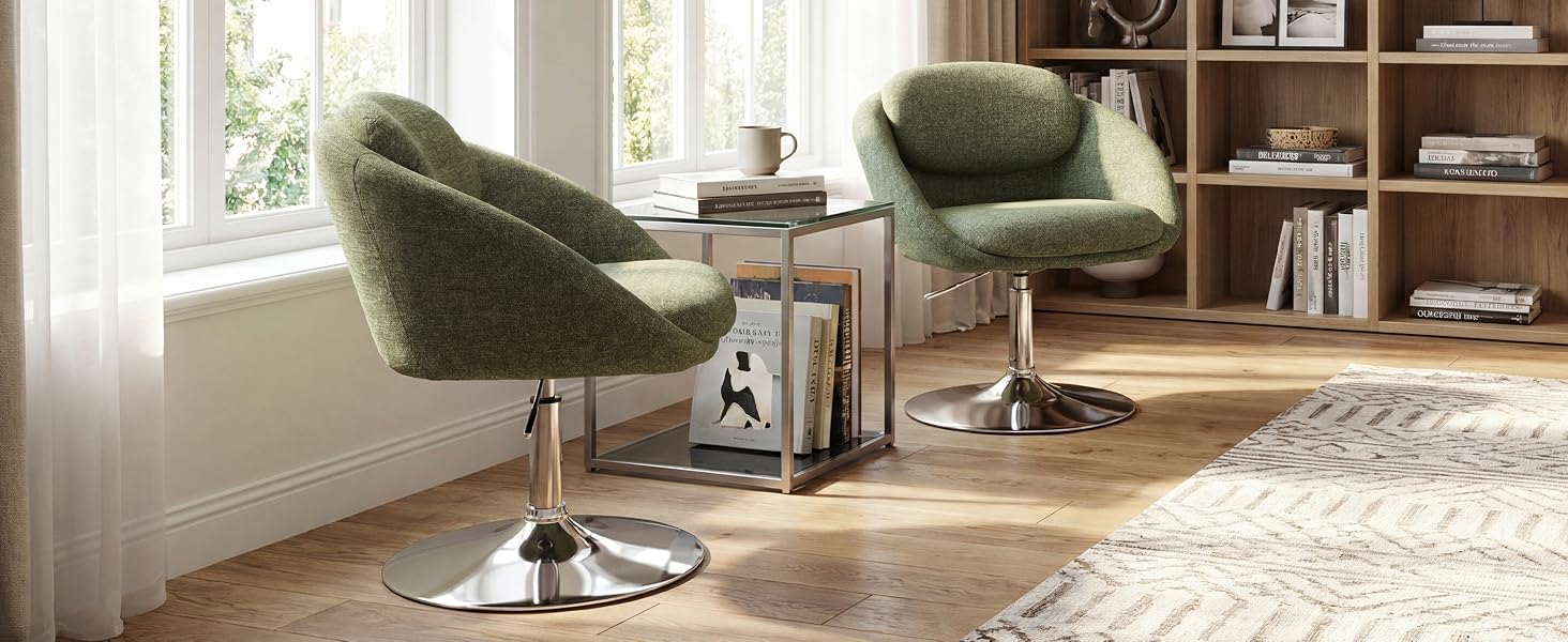 Modern living room interior featuring two green upholstered swivel armchairs positioned near windows, wooden shelving unit with books, area rug, and wooden flooring.