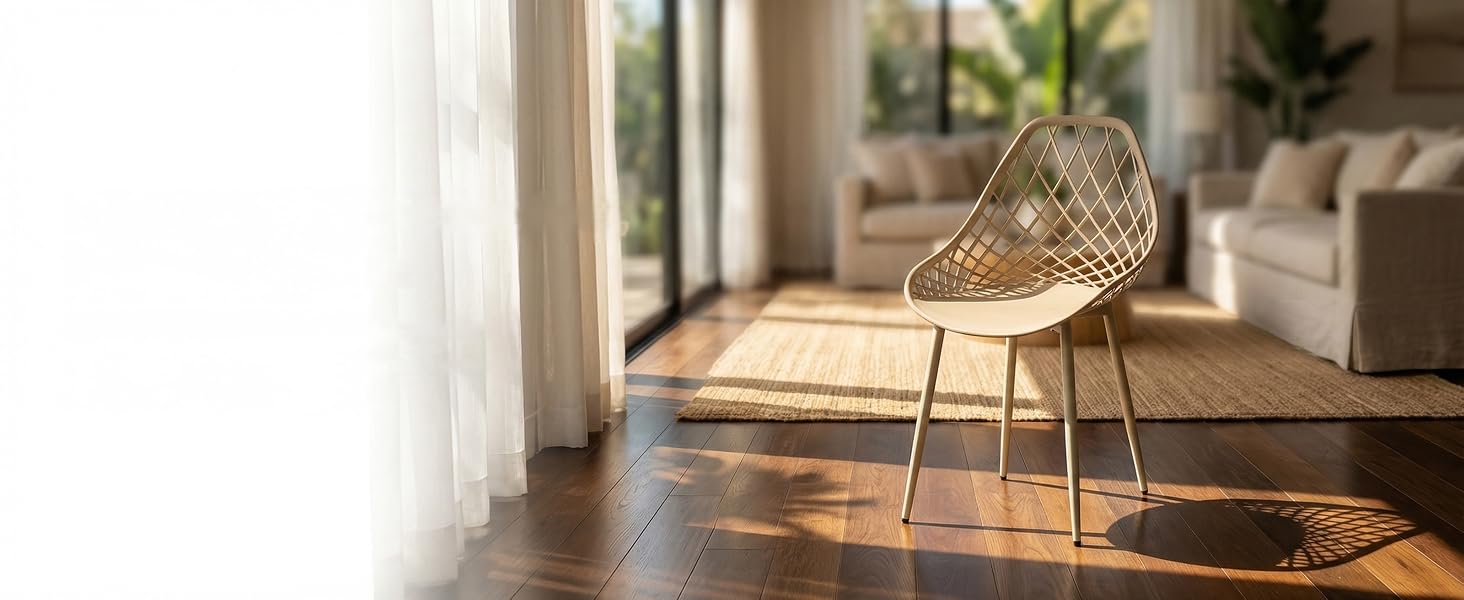 Chaise en osier tressé avec pieds en métal positionnée dans un salon moderne ensoleillé. Plancher en bois naturel, rideaux blancs et meubles neutres visibles en arrière-plan.