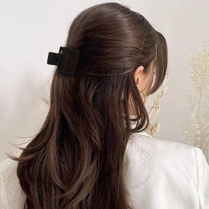 Black rectangular hair clip shown securing back section of long dark hair against light background.