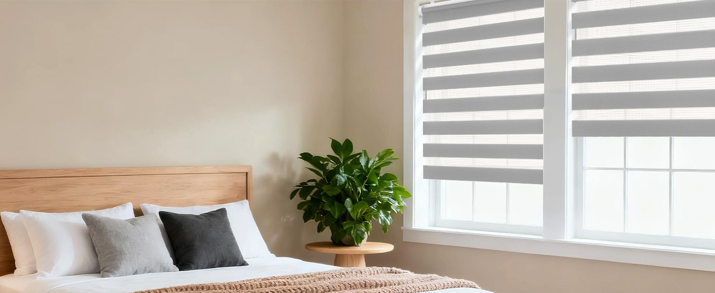 Chambre moderne avec tête de lit en bois, literie grise et blanche, stores de style zèbre et plante en pot dans un coin.