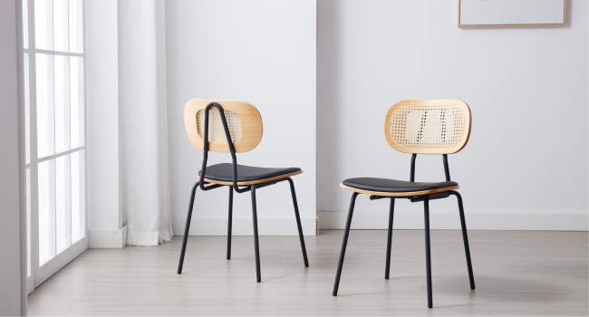 Zwei moderne Esszimmerstühle mit schwarzen Metallrahmen, Holzrückenlehnen mit Stockgeflecht und dunklen gepolsterten Sitzen. Stühle in einer minimalistischen weißen Raumgestaltung