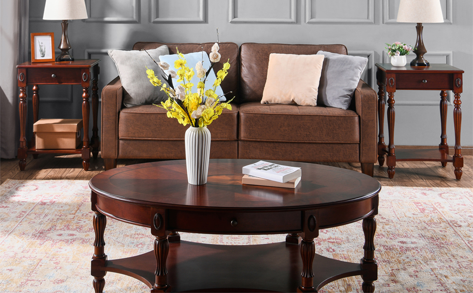 Wohnzimmergarnitur mit braunem Ledersofa, rundem Holzcouchtisch, Beistelltischen mit Lampen und einer Vase mit gelben Blumen. Möbel im traditionellen Stil auf einem gemusterten Teppich.