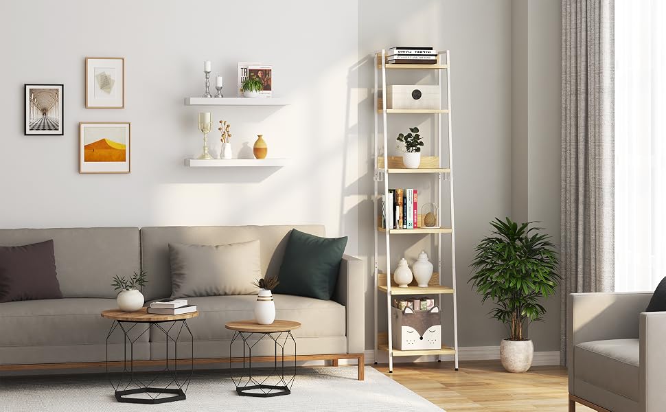 Moderna sala de estar con paredes blancas, con un sofá gris, una mesa de café y una estantería blanca alta. La decoración incluye arte enmarcado, plantas y objetos decorativos