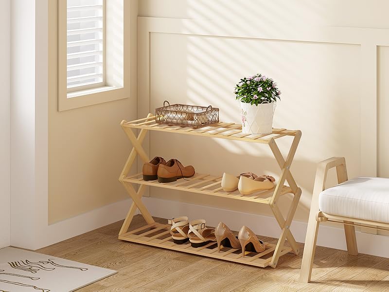 Three-tier wooden shoe rack in a light-colored room corner, holding various shoes and a small plant on the top shelf near a window.