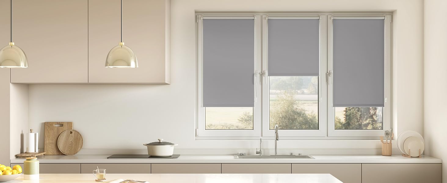 Interior de cocina moderno con cortinas enrollables de color gris claro en las ventanas, gabinetes blancos y combinación de colores neutros.