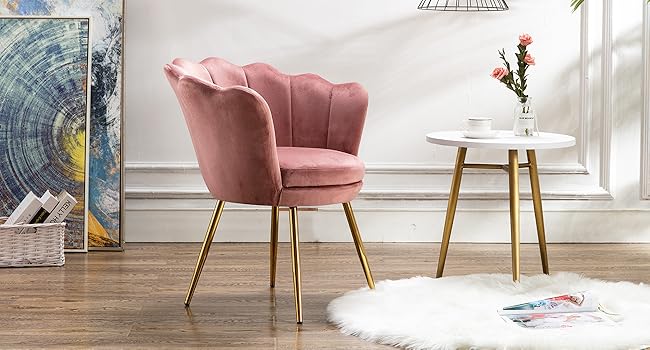 en velours rose avec dossier festonné et pieds en métal doré, placé à côté d'une table d'appoint ronde blanche dans une pièce lumineuse