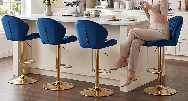 Set of four navy blue velvet bar stools with channel tufting and gold-toned bases, arranged in modern white kitchen setting.