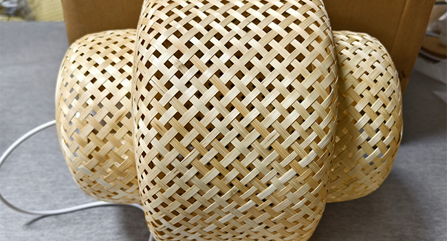 Lampenschirm aus gewebtem Bambus oder Rattan mit filigranem Gittermuster, das eine geschwungene geometrische Struktur in natürlicher Beigefarbe zeigt.
