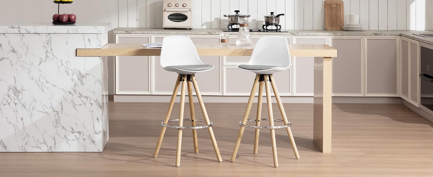 Cocina moderna con isla de mármol, barra de desayuno de madera y dos taburetes blancos con patas de madera. Electrodomésticos y artículos decorativos visibles en las encimeras en segundo plano