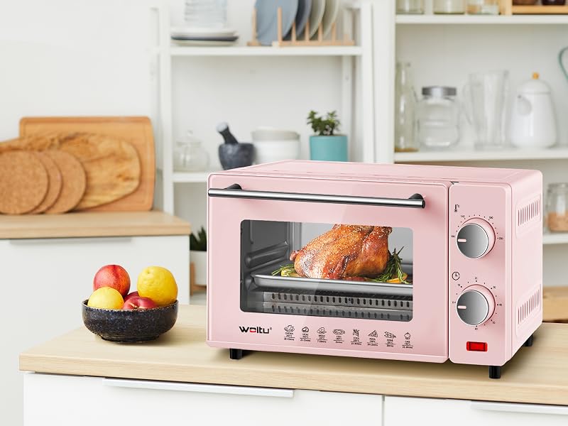 Forno tostapane da banco rosa con pollo arrosto all'interno, esposto in un ambiente da cucina con vari utensili da cucina e frutta