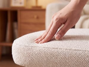 Gros plan de la main appuyant sur un matelas rembourré ou une surface rembourrée gris clair ou crème, démontrant une compression douce et confortable.