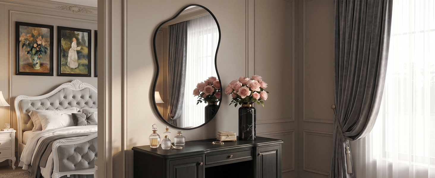 L'intérieur de la chambre comprend un miroir mural ondulé foncé, une tête de lit capitonnée blanche avec des rideaux foncés, une table de chevet avec un arrangement floral, des œuvres d'art encadrées et une palette de couleurs neutres.
