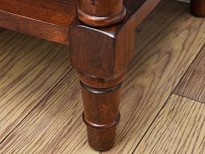 Nahaufnahme eines gedrechselten Möbelbeins aus Holz mit dekorativen Details, das auf einem Holzboden ruht. Das Bein hat eine satte braune Oberfläche