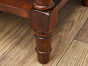 Gros plan d'un pied de meuble en bois tourné avec des détails décoratifs, posé sur un plancher en bois franc. La jambe a une finition brune riche.