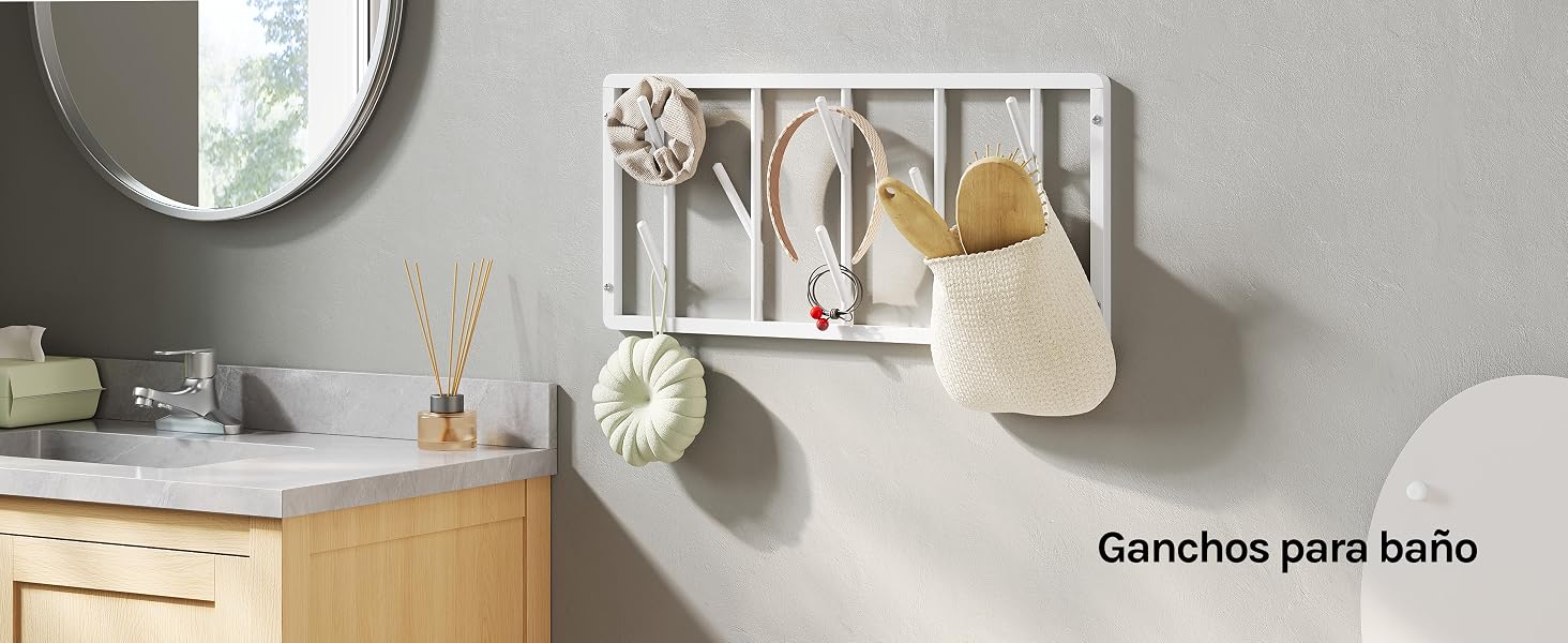 El texto dice «Ganchos para baño» (ganchos para baño). Expositor de pared con ganchos de metal cromado con objetos decorativos colgados, montado en una pared de color beige claro junto a muebles de madera.