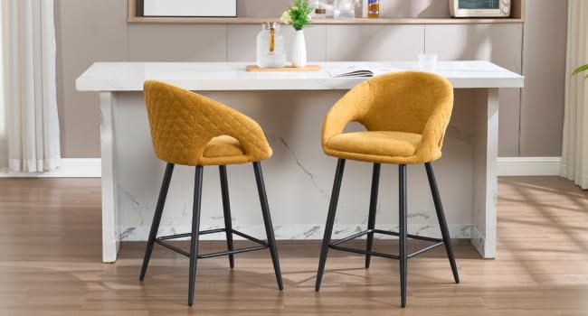 Deux tabourets de bar rembourrés jaune moutarde avec dossiers incurvés et pieds en métal noir, placés sur un comptoir de cuisine blanc ou un îlot.