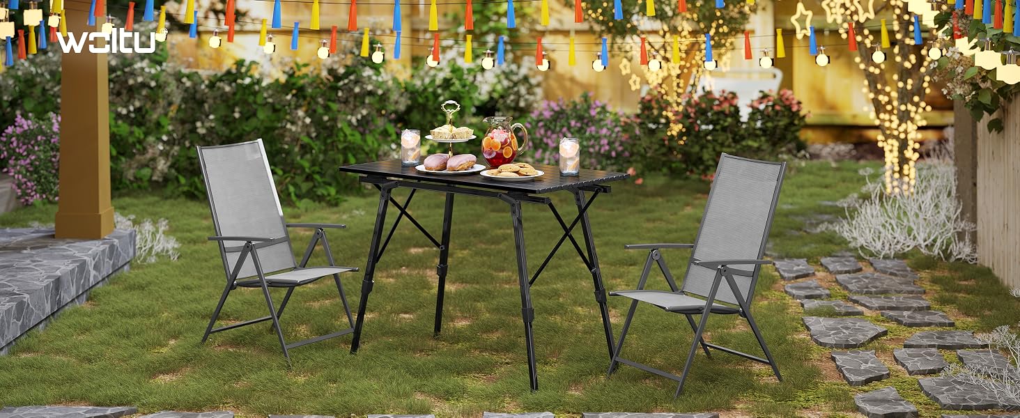 Mobili da giardino per esterni ambientati in giardino, con tavolo rotondo e due sedie pieghevoli sull'erba, circondati da piante e fogliame.