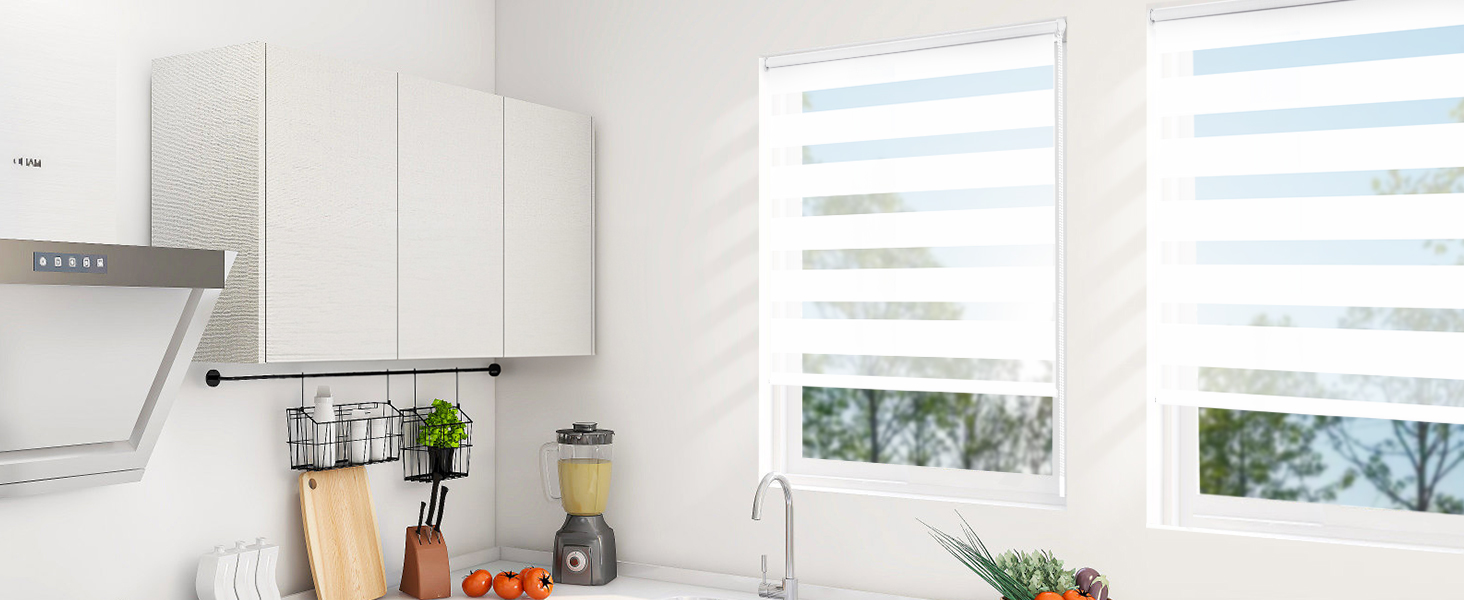 Cuisine blanche moderne avec armoires élégantes, appareils électroménagers en acier inoxydable et grandes fenêtres avec stores réglables. Le plan de travail contient des accessoires de cuisine et des fruits