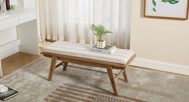 Modern entryway bench with white cushioned seat and wooden frame, styled with small plant.