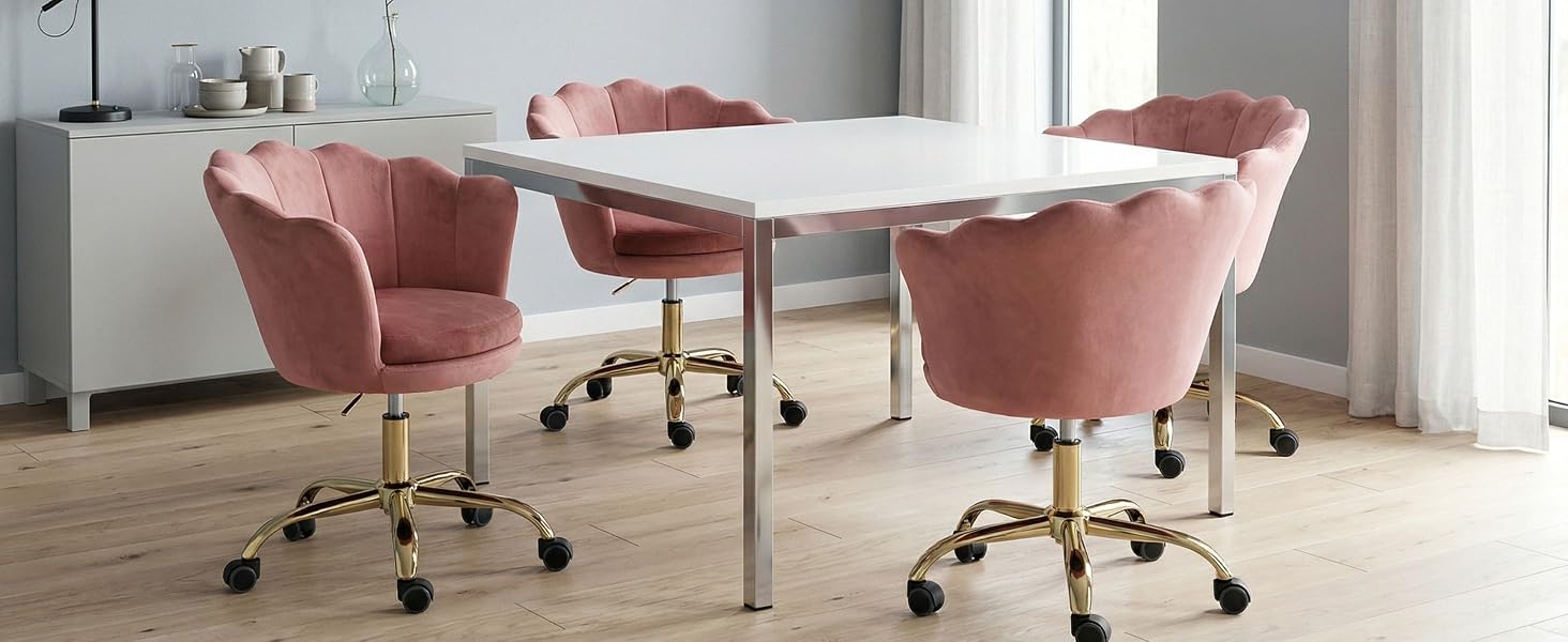 Cadre de bureau moderne avec table blanche et quatre chaises rembourrées en velours rose sur des bases à roulettes dorées. Design intérieur épuré et minimaliste.