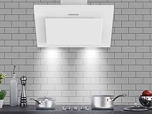 Hotte de cuisine inclinée blanche montée au-dessus du poêle sur un mur carrelé. Ustensiles de cuisine en acier inoxydable visibles sur la table de cuisson ci-dessous