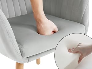 Demonstration of chair upholstery softness and cushioning, showing hand pressing into light gray fabric seat with detailed close-up inset.