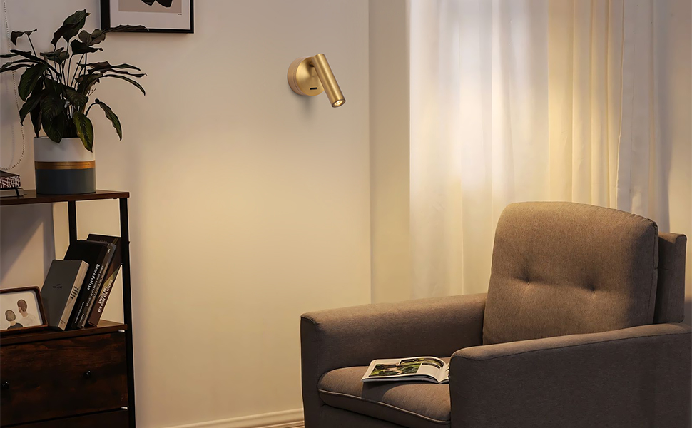 Coin salon confortable avec un fauteuil gris, une applique dorée et une table d'appoint en bois. Un éclairage tamisé crée une ambiance chaleureuse.