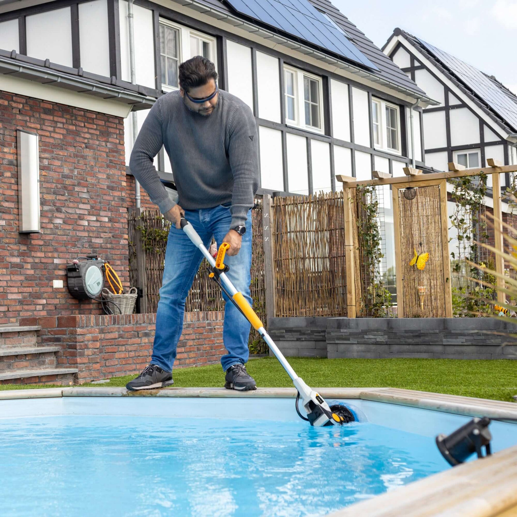 Photo montrant l'utilisation de la Twin Brush pour nettoyer les parois d'une piscine, la brosse étant partiellement sous l'eau