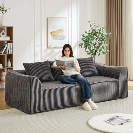 Canapé en tissu cordé minimaliste, avec des lignes sinueuses et un dossier qui s’incline doucement vers l’arrière. Il est équipé de deux coussins. (1/5)