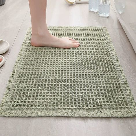 Questo tappeto verde a nido d'ape è realizzato in microfibra morbida, resistente e altamente assorbente. È dotato di un retro in gomma antiscivolo ed è decorato con pon-pon. Lavabile in lavatrice, mis