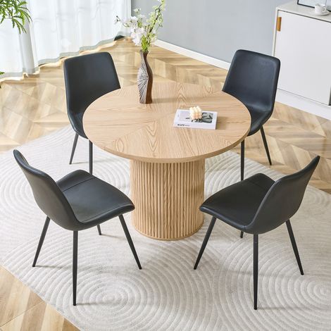 Ensemble minimaliste composé d'une table ronde et de quatre chaises. Table de salle à manger ronde en MDF de 100 cm de diamètre, aspect bois clair. Chaises assorties, revêtues de similicuir noir. (1/4)