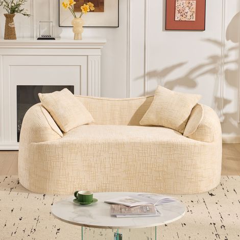 Sofá de compresión curvo de dos plazas en color beige con reposabrazos y dos cojines. Ideal para apartamentos pequeños, salones o dormitorios.