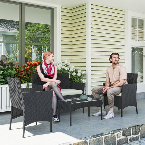 Set di mobili da giardino in rattan sintetico con divano, poltrone, tavolo in vetro temperato e cuscini nei colori nero e crema.