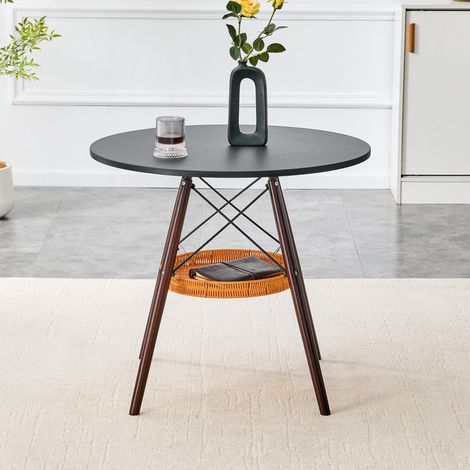 Ein runder Esstisch mit einem Durchmesser von 80 cm, einer Tischplatte aus schwarzem MDF und Tischbeinen aus walnussfarbenem Massivholz, ergänzt durch ein schwebendes, geflochtenes Ablagefach. (1/5)